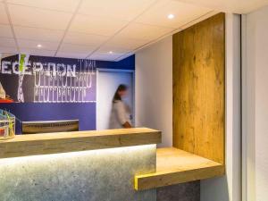 a restaurant with a wooden counter and a person in the background at Ibis Budget Angers Parc des Expositions in Saint-Sylvain-dʼAnjou