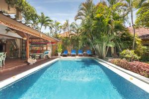 a swimming pool with palm trees and a house at Villa Kaja by Nagisa Bali in Seminyak
