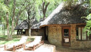 a stone house with a thatched roof with chairs outside at Sable Creek Safari Lodge in Tzaneen
