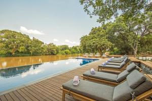 a row of lounge chairs on a wooden deck next to a river at Abelana River Lodge in Phalaborwa