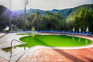 uma piscina de água verde com cadeiras e montanhas ao fundo em Grand Hotel Delle Terme em Terme Luigiane