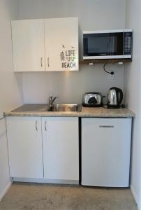 a kitchen with white cabinets and a sink and a microwave at In the Heart of the Beach in Waihi Beach