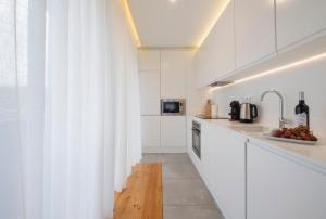 a white kitchen with white cabinets and a wooden floor at Aqua - Pópulo Eco Village in Ponta Delgada