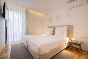 a white bedroom with a large bed and a television at Aqua - Pópulo Eco Village in Ponta Delgada