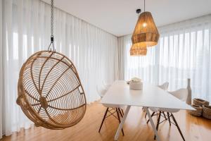 a dining room with a white table and a rattan chair at Aqua - Pópulo Eco Village in Ponta Delgada