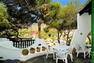 a white patio with a table and chairs and trees at Hostal Los Pinos in Cala de Sant Vicenc