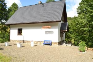 a white barn with a black roof and a blue bench at Trzy Strumyki in Kąty Bystrzyckie
