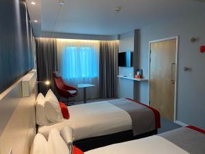 a hotel room with two beds and a red chair at Holiday Inn Express Ramsgate – Minster by IHG in Minster