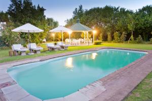 a swimming pool in a backyard with a table and umbrellas at Oue Werf Country House in Oudtshoorn