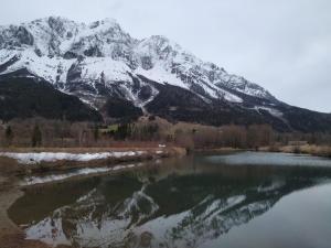 uma montanha coberta de neve é refletida em uma massa de água em Pension Tilly em Niederöblarn