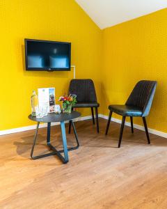 Duas cadeiras e uma mesa com uma televisão numa parede amarela em Hotel Brasserie de Huifkar em Middelburg