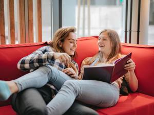 two girls sitting on a red couch reading books at ibis Hotel München City in Munich