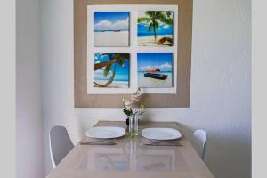 einen Esstisch mit zwei weißen Tellern und Bildern an der Wand in der Unterkunft AZUR - Séjour FARNIENTE en Guadeloupe! in Le Gosier