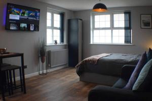 a bedroom with a bed and a couch and two windows at The Den Studio Apartment - Withernsea in Withernsea