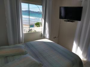 a bedroom with a bed and a window with a television at Casa Beira Mar Mariscal Superior in Bombinhas