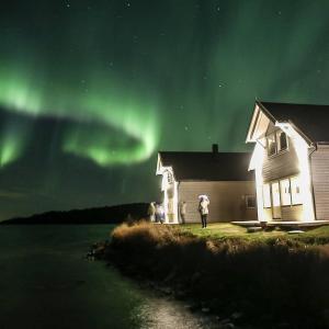 a person standing in front of a house under the aurora at Senja arctic lodge in Stonglandseidet