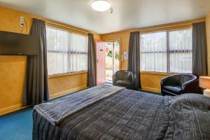 a bedroom with a bed and two chairs and windows at Red Tussock Motel in Te Anau
