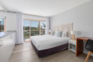a white bedroom with a bed and a large window at Charlesworth Bay Beach Resort in Coffs Harbour