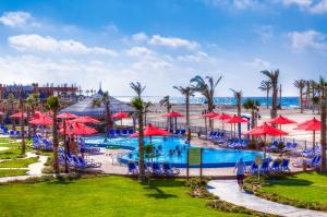 a resort pool with red umbrellas and a beach at Porto Matrouh Beach Resort in Marsa Matruh