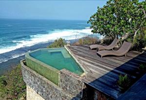 a swimming pool on a wooden deck next to the ocean at Batu Hill Villa in Watukarung