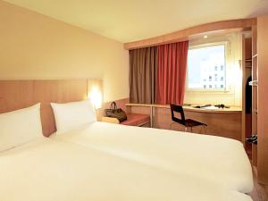 um quarto de hotel com uma grande cama branca e uma secretária em Hotel ibis Lisboa Jose Malhoa em Lisboa