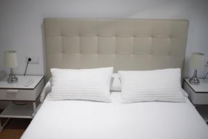 uma cama branca com duas almofadas brancas e uma cabeceira em Apartamento Noia Centro Izqda em Noya