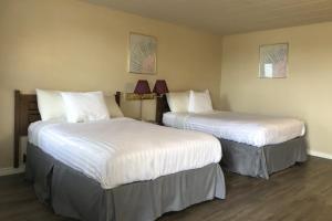 two beds in a hotel room with white sheets at Knights Inn Fort Erie in Fort Erie