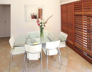 a glass dining room table with white chairs and a vase of flowers at Onetangi Beach Apartments in Onetangi