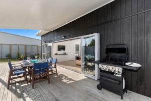 eine Terrasse mit einem Tisch und einem Grill sowie einem Tisch und Stühlen in der Unterkunft The Sunshine Bungalow - Mangawhai Heads Home in Mangawhai + 19 Fotos