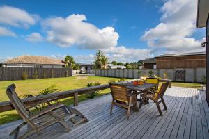 eine Holzterrasse mit einem Tisch und Stühlen darauf in der Unterkunft The Sunshine Bungalow - Mangawhai Heads Home in Mangawhai