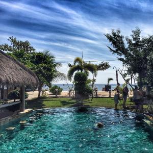 a swimming pool in front of a beach with people at Puri Air Beach Resort & Spa in Gili Air