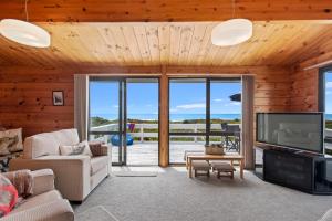 ein Wohnzimmer mit einem großen TV und Glasschiebetüren in der Unterkunft Oceanside Bach - Mount Maunganui Holiday Home in Mount Maunganui