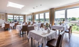 restauracja z białymi stołami, krzesłami i oknami w obiekcie Hotel Swiss Star w mieście Wetzikon