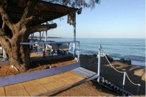 a porch with a table and a tree next to the ocean at Studios Akrogiali in Kyparissia