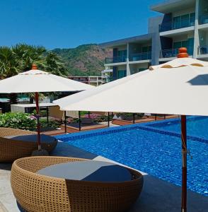 a swimming pool with umbrellas and chairs next to a building at Sugar Palm Grand Hillside - SHA Plus in Kata Beach