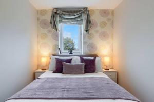 a bedroom with a bed with purple pillows and a window at 45 Guthrie Court, Fantastic top floor apartment next to Gleneagles in Auchterarder
