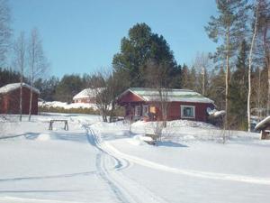 a snow covered road leading to a red cabin at Holiday Home Raanumökki 1 by Interhome in Lampsijärvi