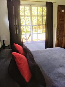 a bed with red and black pillows in front of a window at Posada Quinta Pata in Ezeiza