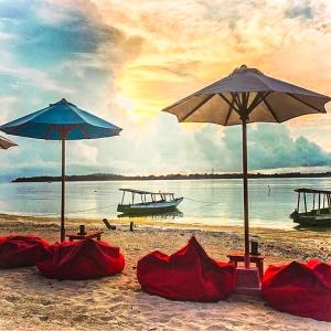 una spiaggia con due ombrelloni e coperte rosse sulla sabbia di Pandan Bungalow a Gili Air