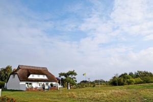 a white house with a brown roof in a field at Ferienzimmer unterm Reetdach in Pl in Neuendorf