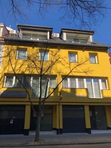 un edificio amarillo con un árbol delante de él en Mosoly Szallashely, en Szeged