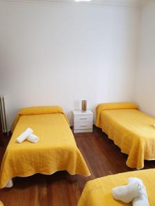 two beds in a room with yellow covers and wooden floors at Pensión Hedrass in Santiago de Compostela