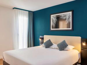 a bedroom with a large white bed with blue walls at Aparthotel Adagio Monaco Palais Joséphine in Beausoleil