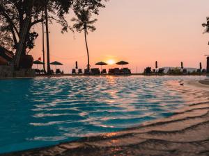 ein Swimmingpool mit einem Sonnenuntergang im Hintergrund in der Unterkunft Frangipani Langkawi Resort in Pantai Cenang
