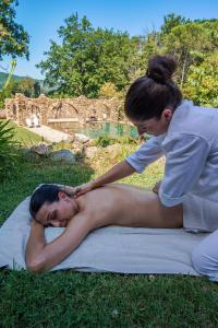 Eine Frau, die auf dem Gras liegt, während eine Frau einer Frau eine Massage gibt. in der Unterkunft La Cerreta - Terme di Sassetta in Sassetta