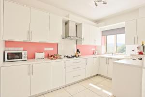a white kitchen with pink walls and white cabinets at Villa Georgios Rafaela in Polis Chrysochous