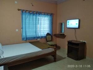 a bedroom with a bed and a tv and a chair at Aruvi Hotel in Yelagiri