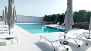 una piscina con sillas y sombrillas blancas en Ulivo Apartment, en Locorotondo