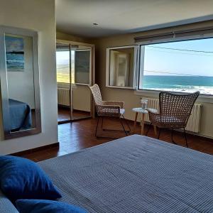 a bedroom with a bed and chairs and a view of the ocean at Hostal Balieiros Corrubedo in Corrubedo