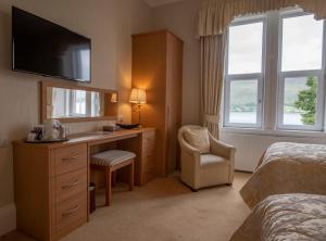 a hotel room with a bedroom with a desk and a tv at Myrtle Bank Guest House in Fort William